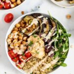 Colorful quinoa bowls topped with roasted red pepper sauce and fresh Mediterranean ingredients.