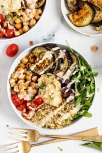 Colorful quinoa bowls topped with roasted red pepper sauce and fresh Mediterranean ingredients.