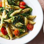 Bowl of penne pasta coated in vibrant green pesto sauce.