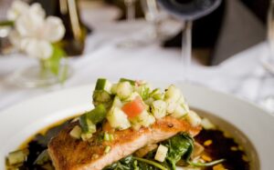 Perfectly seared salmon fillet alongside bright green broccolini on a white plate, drizzled with golden lemon garlic caper sauce and garnished with fresh parsley