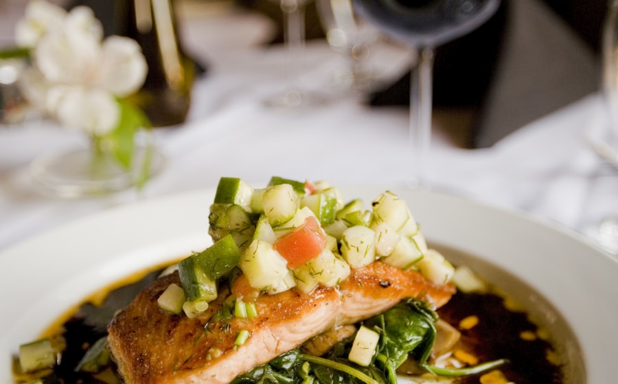Close-up shot of flaky salmon with a forkful being lifted, showing the perfectly cooked interior alongside vibrant green broccolini