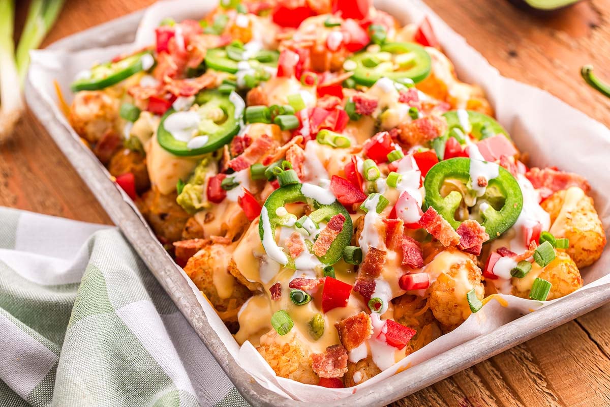 loaded tater tot nachos on large platter with melted cheese, ground beef, jalapeños, and fresh toppings