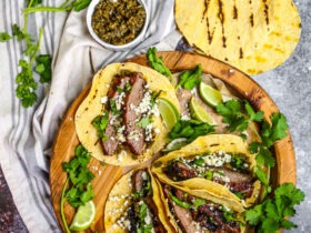 Perfectly grilled carne asada tacos garnished with fresh cilantro, diced onions, and lime wedges on a wooden serving board
