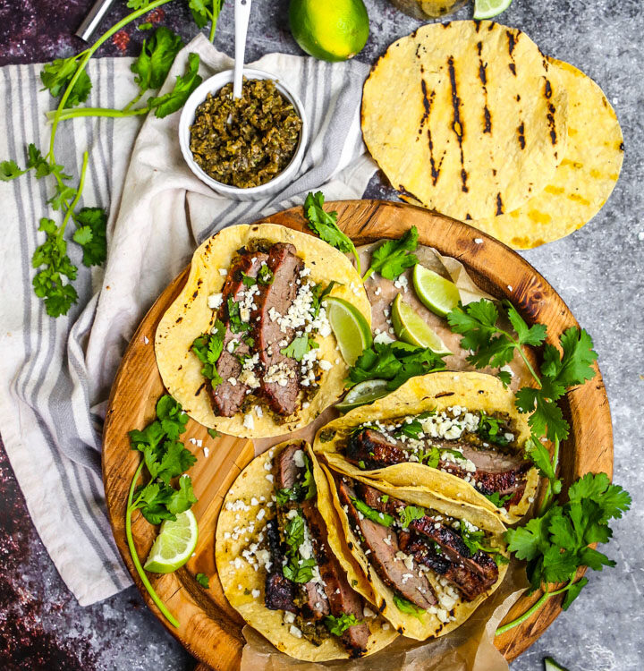 Perfectly grilled carne asada tacos garnished with fresh cilantro, diced onions, and lime wedges on a wooden serving board