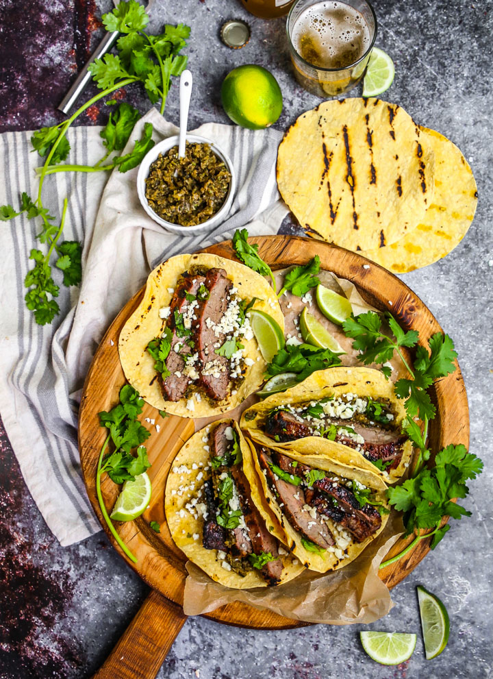 Perfectly grilled carne asada tacos garnished with fresh cilantro, diced onions, and lime wedges on a wooden serving board