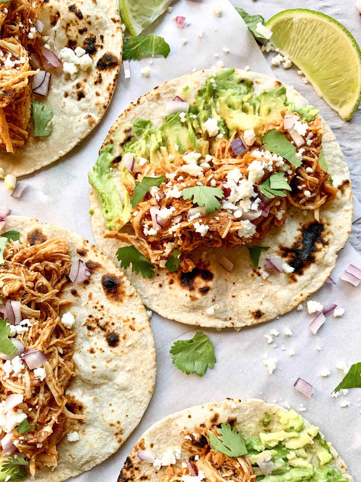 Close-up shot of chicken tinga in a warm flour tortilla garnished with fresh cilantro, crumbled queso fresco, and lime wedges
