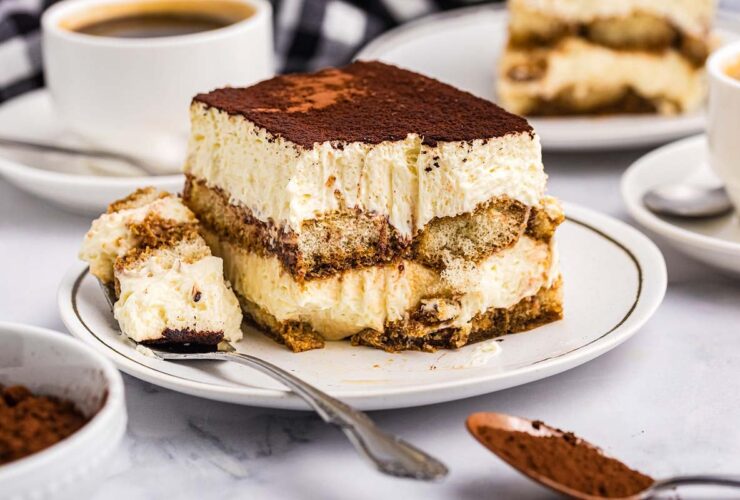 Classic tiramisu in glass dish with cocoa powder dusting and coffee beans scattered around