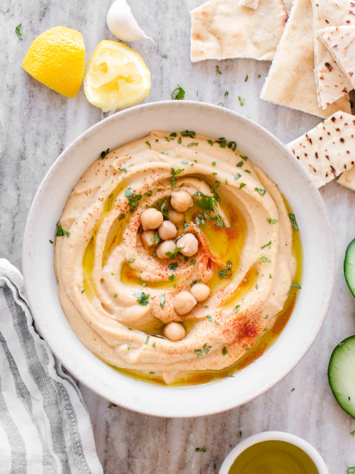 Smooth and creamy homemade hummus in a white bowl, drizzled with golden olive oil and sprinkled with paprika, surrounded by fresh vegetables and warm pita bread