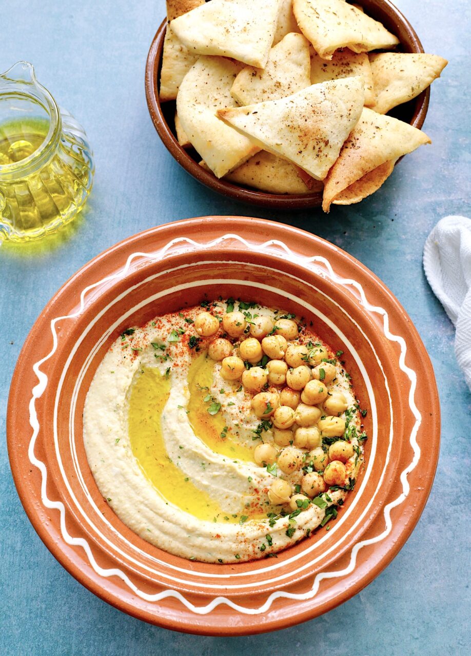 Close-up shot of creamy hummus being scooped with a pita chip, showing the smooth, velvety texture and golden olive oil drizzle on top