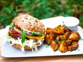 Tender, juicy pulled pork piled high on a brioche bun with coleslaw, served alongside crispy sweet potato fries on a rustic wooden plate