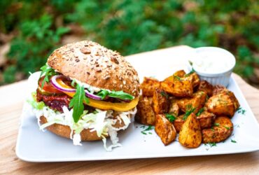 Tender, juicy pulled pork piled high on a brioche bun with coleslaw, served alongside crispy sweet potato fries on a rustic wooden plate