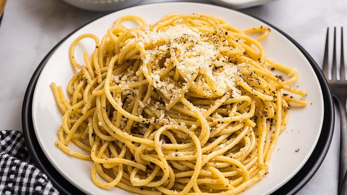 Close-up of silky cacio e pepe pasta being twirled on a fork with visible black pepper specks