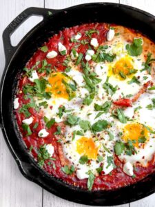 Shakshuka served in cast iron skillet with golden egg yolks and fresh herbs, garnished with crumbled feta and served with crusty bread