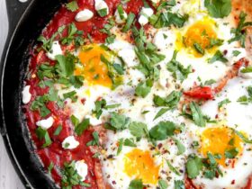 Shakshuka served in cast iron skillet with golden egg yolks and fresh herbs, garnished with crumbled feta and served with crusty bread