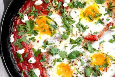 Shakshuka served in cast iron skillet with golden egg yolks and fresh herbs, garnished with crumbled feta and served with crusty bread