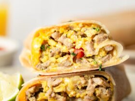 High protein scrambled egg breakfast burrito cut in half on a white plate, showing the colorful filling with fluffy scrambled eggs, melted cheese, and fresh vegetables, garnished with cilantro and served with salsa on the side