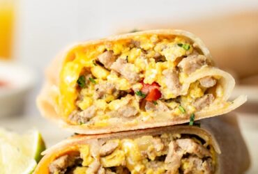 High protein scrambled egg breakfast burrito cut in half on a white plate, showing the colorful filling with fluffy scrambled eggs, melted cheese, and fresh vegetables, garnished with cilantro and served with salsa on the side