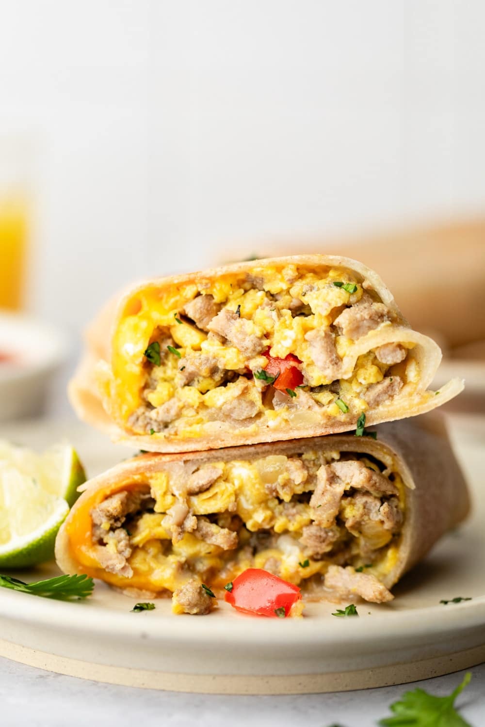 High protein scrambled egg breakfast burrito cut in half on a white plate, showing the colorful filling with fluffy scrambled eggs, melted cheese, and fresh vegetables, garnished with cilantro and served with salsa on the side
