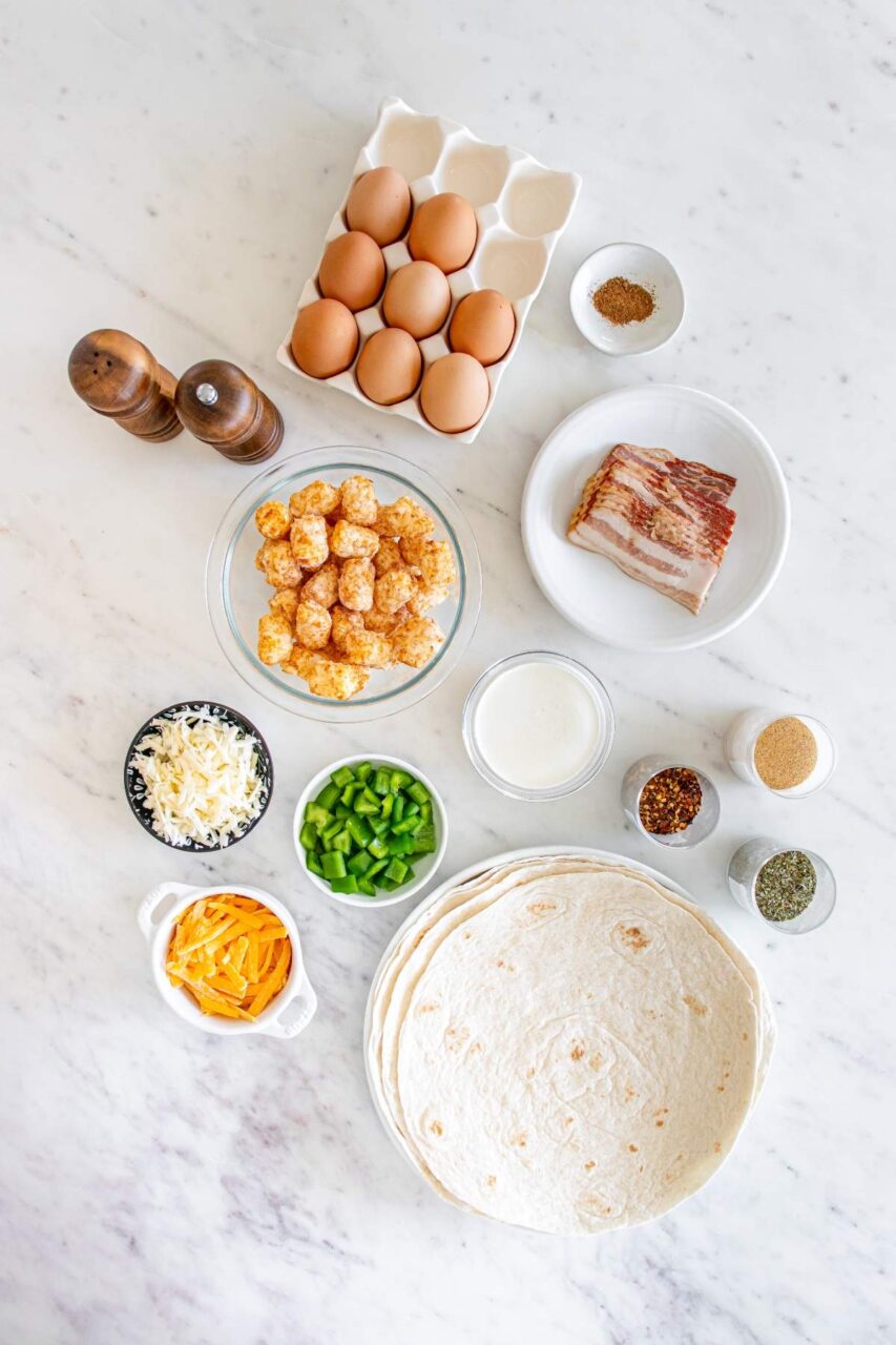 Ingredients laid out for high protein breakfast burrito including whisked eggs with Greek yogurt, grated cheese, diced vegetables, and large flour tortillas on a marble countertop