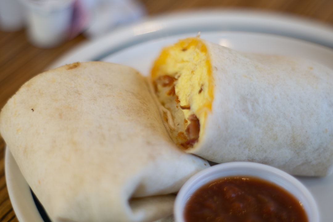 Close-up cross-section view of the high protein breakfast burrito showing layers of fluffy scrambled eggs, melted cheese, and colorful vegetables, with a small bowl of fresh salsa and sliced avocado on a rustic wooden board