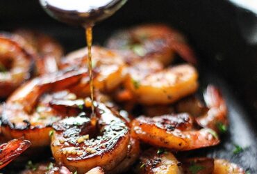 honey glazed shrimp in skillet with golden caramelized sauce and garnished with green onions and sesame seeds