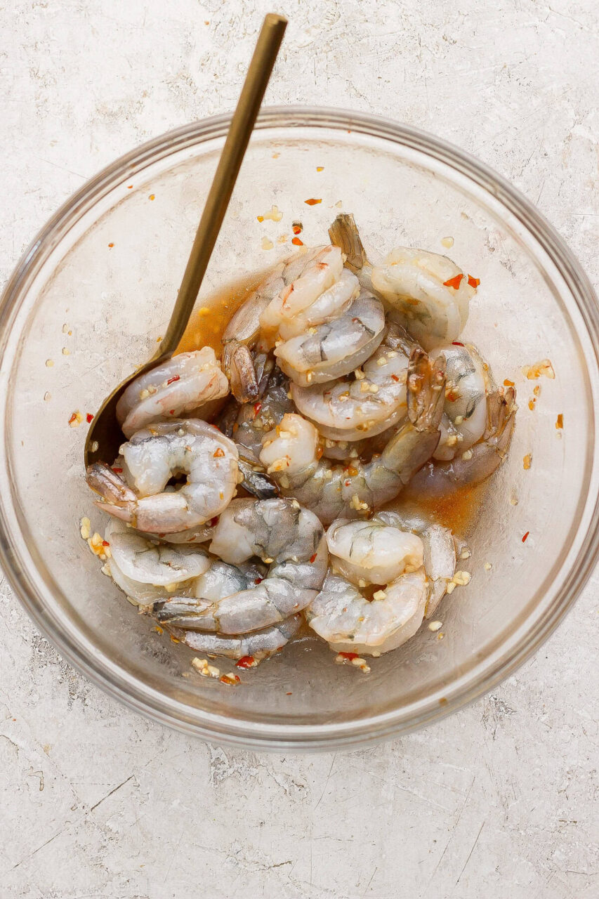 raw shrimp being marinated with garlic, honey, and soy sauce in a glass bowl