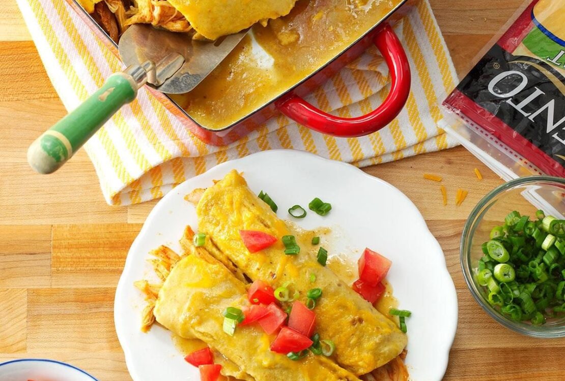 Golden honey lemon chicken enchiladas in a white baking dish, garnished with fresh cilantro and lemon wedges, showing the caramelized tops