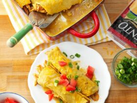 Golden honey lemon chicken enchiladas in a white baking dish, garnished with fresh cilantro and lemon wedges, showing the caramelized tops