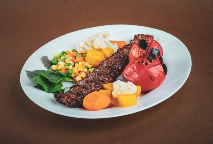 Lebanese kafta kebabs beautifully plated on a white serving platter with grilled vegetables, fresh parsley garnish, and pita bread on the side