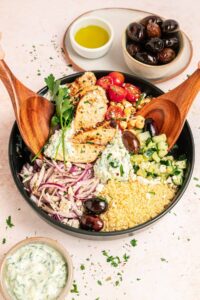 Mediterranean chicken bowl with golden seasoned chicken, fresh vegetables, olives, feta cheese, and creamy tzatziki arranged in a rustic ceramic bowl