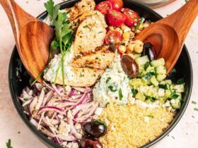 Mediterranean chicken bowl with golden seasoned chicken, fresh vegetables, olives, feta cheese, and creamy tzatziki arranged in a rustic ceramic bowl
