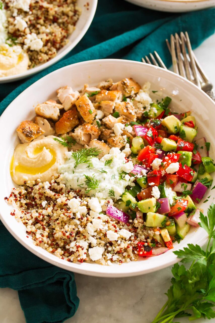 Close-up shot of a Mediterranean chicken bowl showing the golden chicken, vibrant vegetables, and creamy tzatziki drizzle