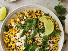 Mexican street corn served in a rustic skillet garnished with fresh cilantro, lime wedges, and crumbled cotija cheese