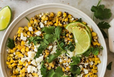 Mexican street corn served in a rustic skillet garnished with fresh cilantro, lime wedges, and crumbled cotija cheese