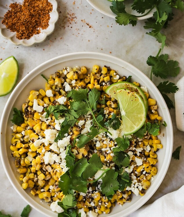 Mexican street corn served in a rustic skillet garnished with fresh cilantro, lime wedges, and crumbled cotija cheese