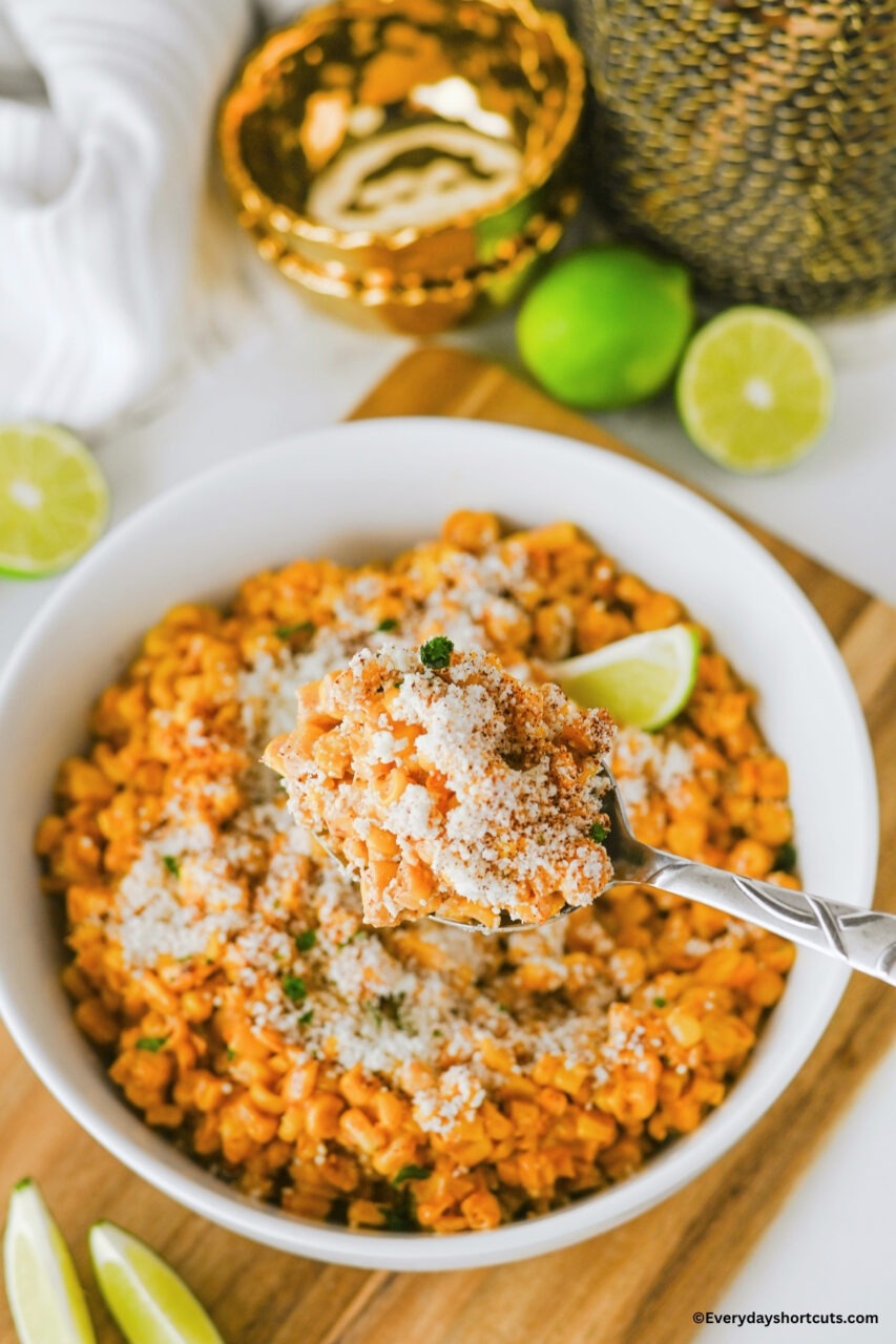 Close-up shot of Mexican street corn in a serving bowl with a wooden spoon, showing the creamy coating and cheese crumbles