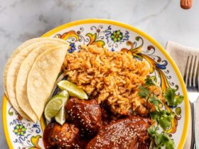 Mole poblano chicken served on white plate garnished with sesame seeds and cilantro with rice on the side