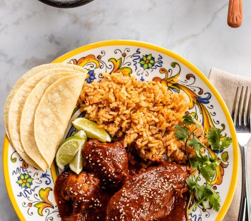 Mole poblano chicken served on white plate garnished with sesame seeds and cilantro with rice on the side
