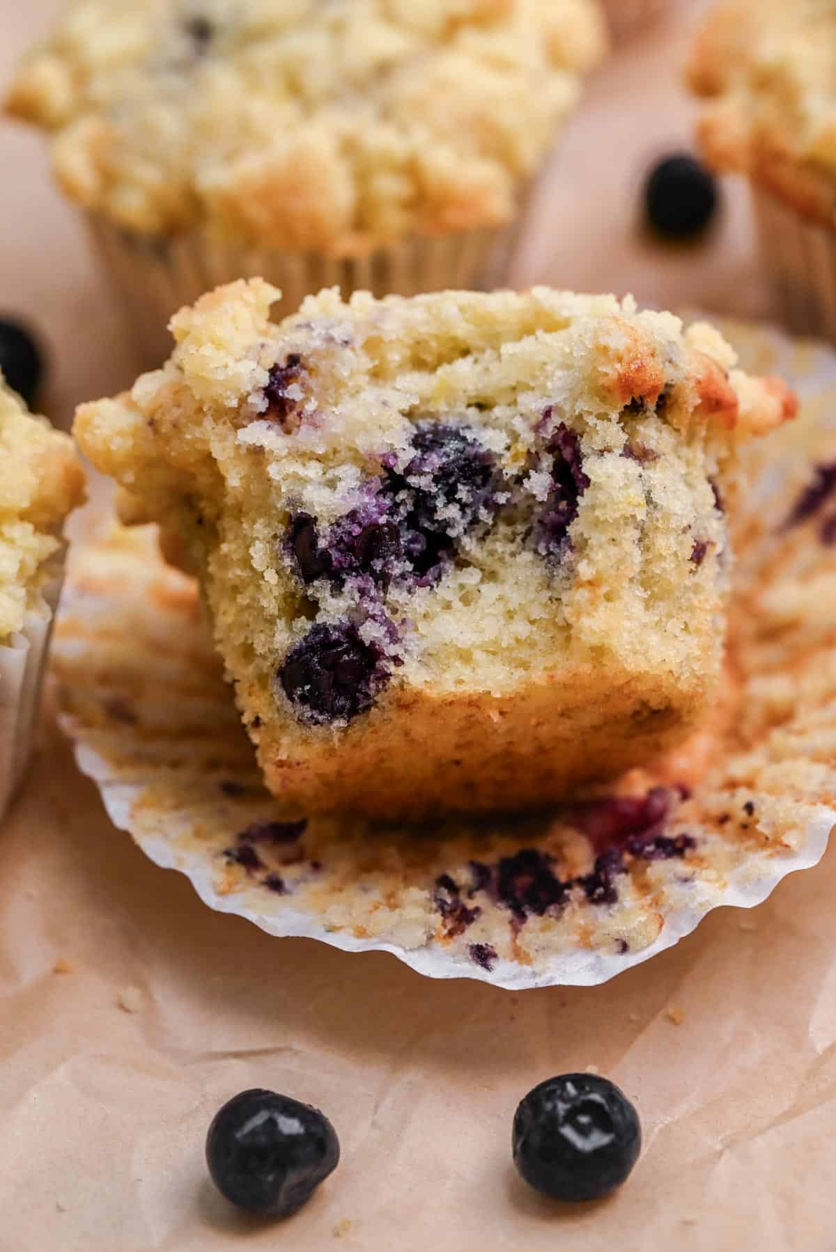 Close-up shot of a split blueberry muffin showing the fluffy interior texture with visible blueberries, served on a white plate with butter and jam nearby