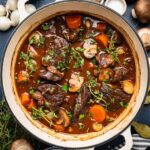 Beef Bourguignon served in a rustic white bowl with tender chunks of beef, mushrooms, and pearl onions in rich burgundy sauce, garnished with fresh thyme