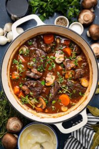 Beef Bourguignon served in a rustic white bowl with tender chunks of beef, mushrooms, and pearl onions in rich burgundy sauce, garnished with fresh thyme