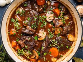 Beef Bourguignon served in a rustic white bowl with tender chunks of beef, mushrooms, and pearl onions in rich burgundy sauce, garnished with fresh thyme