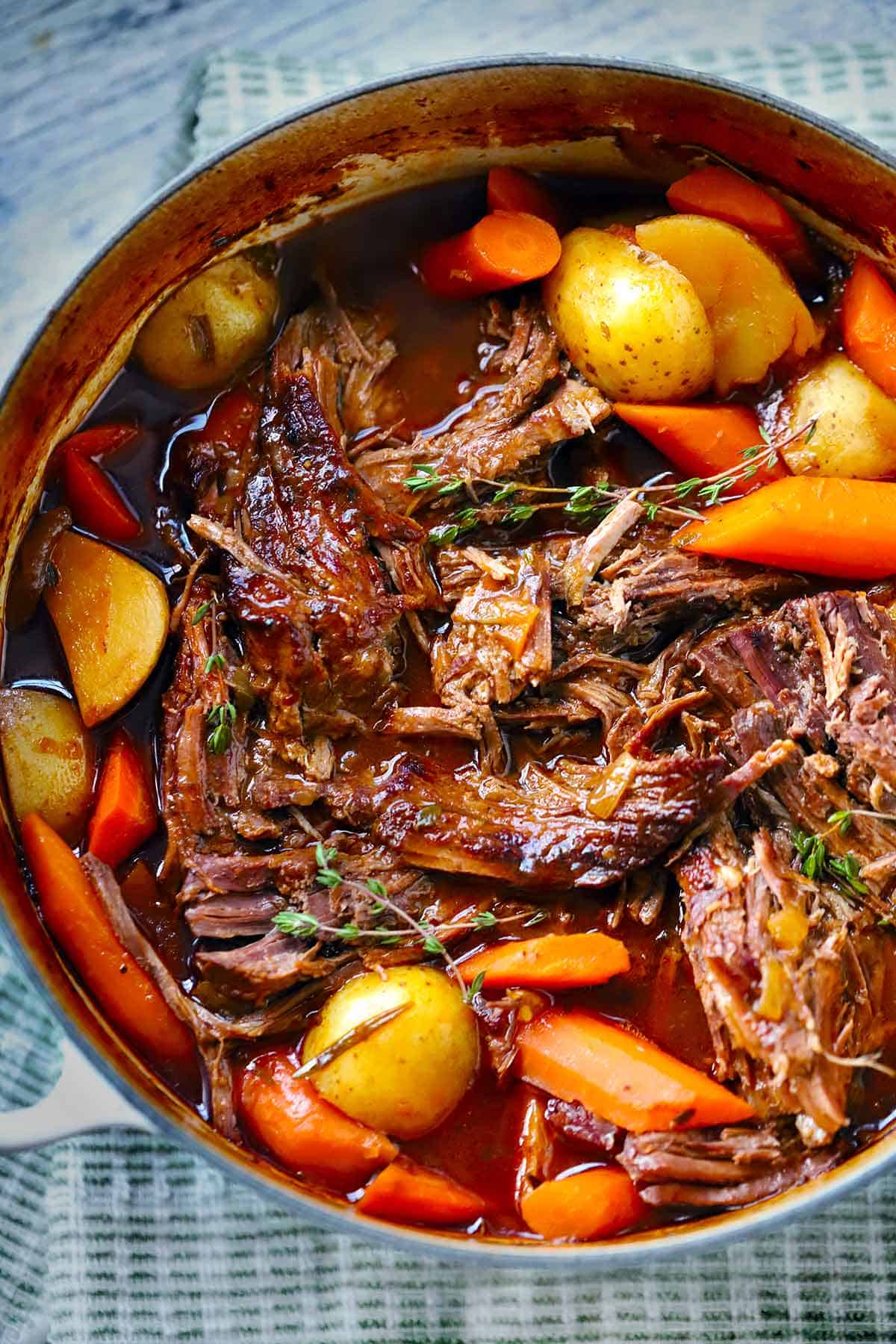 Step-by-step shot showing golden-brown beef chunks being seared in a Dutch oven with diced vegetables and herbs nearby