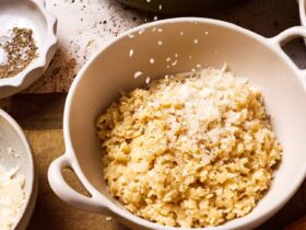 Creamy buttered pastina served in a white ceramic bowl with freshly grated Parmesan cheese and black pepper, garnished with fresh herbs on a rustic wooden table