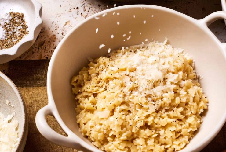 Creamy buttered pastina served in a white ceramic bowl with freshly grated Parmesan cheese and black pepper, garnished with fresh herbs on a rustic wooden table