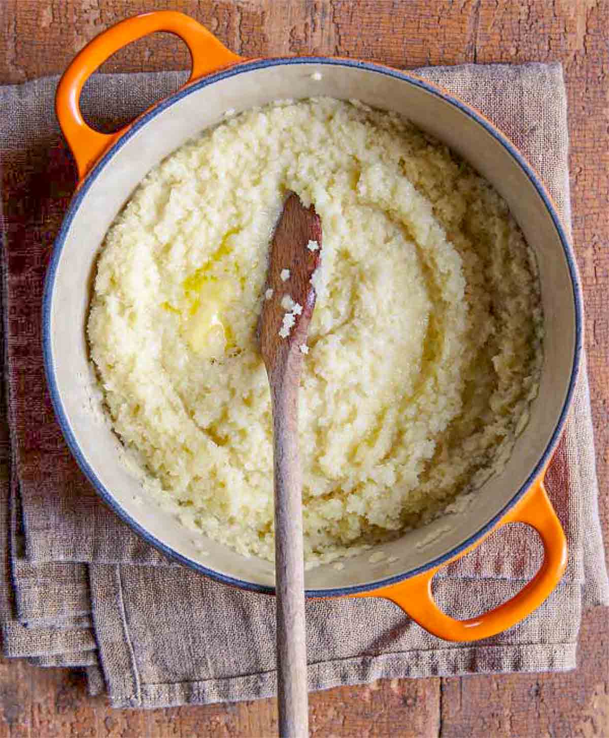 Overhead shot of pastina cooking in a pot with butter being stirred in, showing the creamy, glossy texture forming
