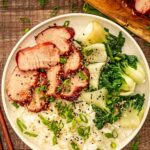 Glossy char siu pork slices arranged on white plate with steamed rice and green onions garnish