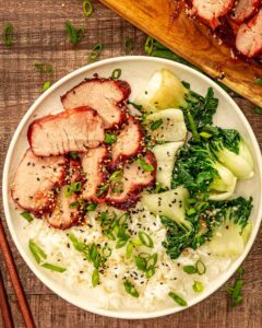 Glossy char siu pork slices arranged on white plate with steamed rice and green onions garnish
