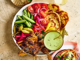 Sliced chicken shawarma on a platter with fresh herbs, pita bread, and colorful vegetables arranged around it