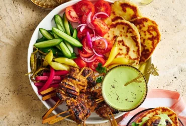 Sliced chicken shawarma on a platter with fresh herbs, pita bread, and colorful vegetables arranged around it